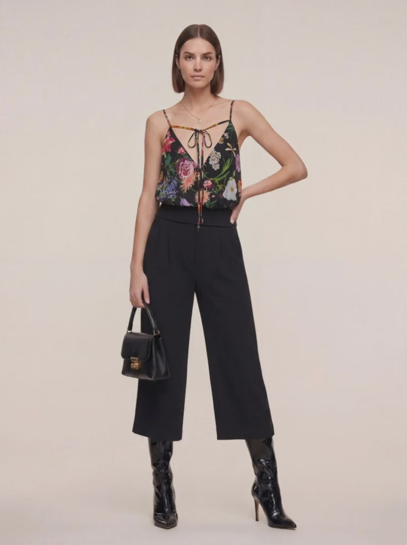 Femme portant un Haut en soie et pantalon noir trois quart et un sac en cuir à la main